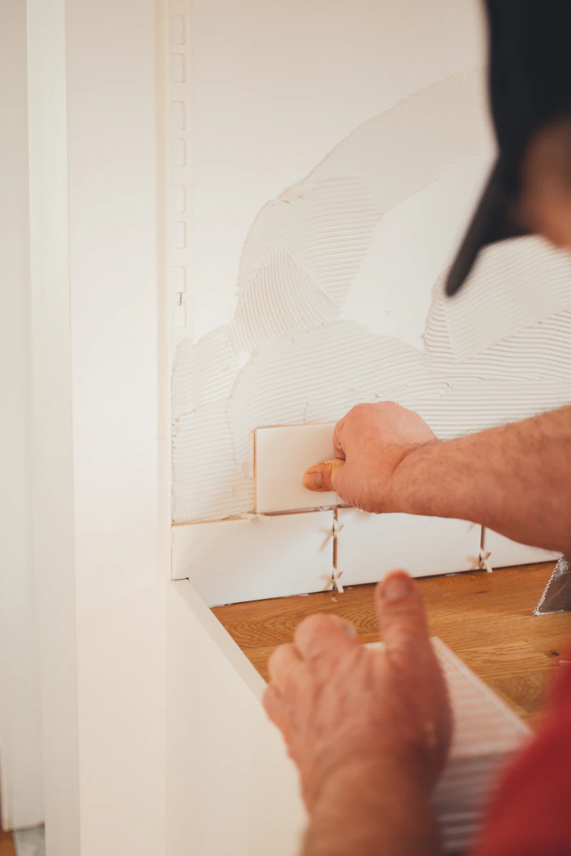 Hände setzen eine weiße Fliese an die Wand